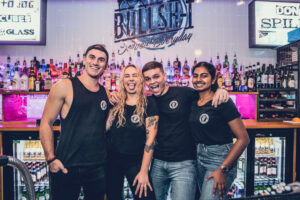 4 young bartenders smile at the camera, in a bar